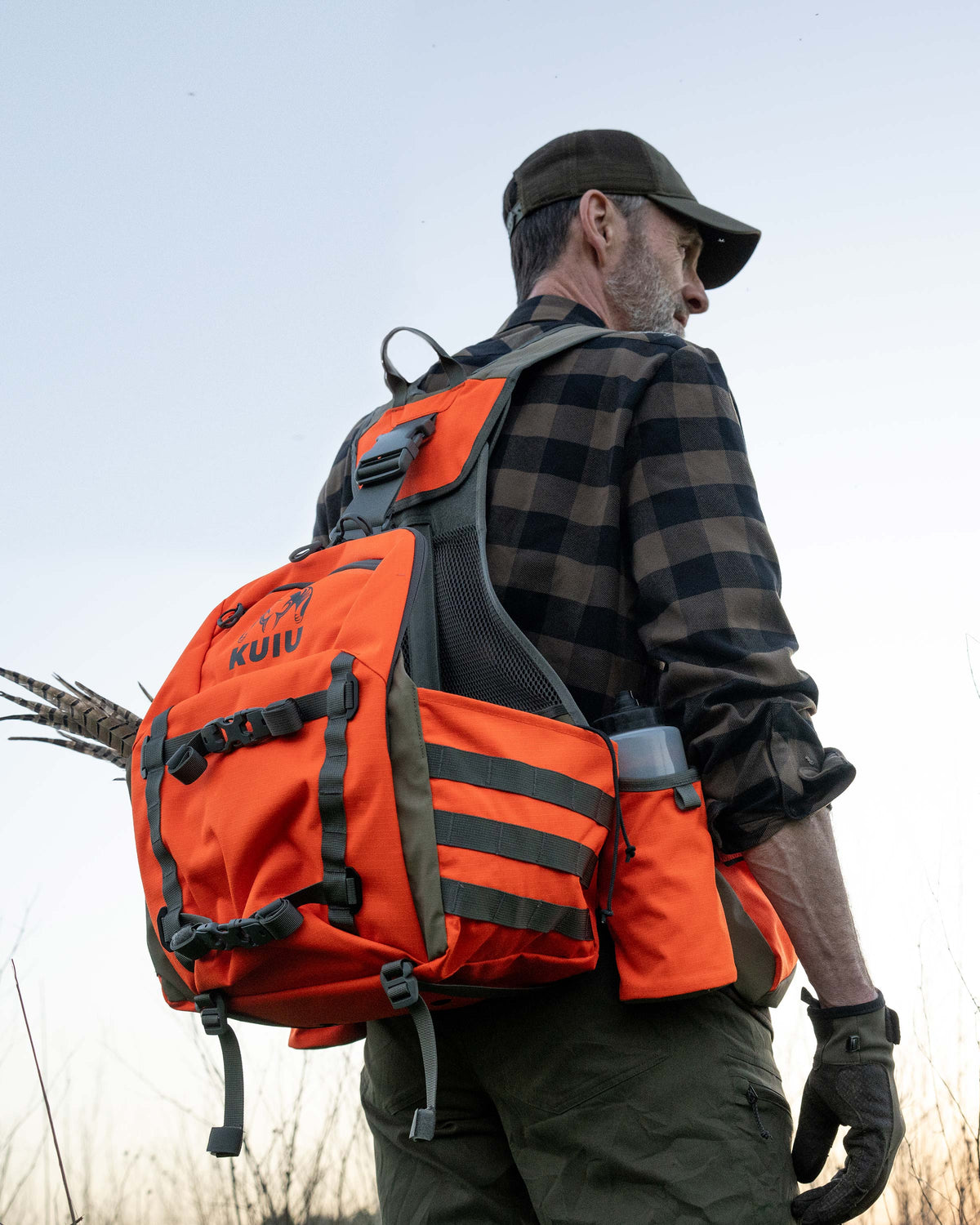 Back angled view of Hunter wearing Upland Field Vest in Blaze Orange with visual of pheasant feathers sticking out of the left side pouch