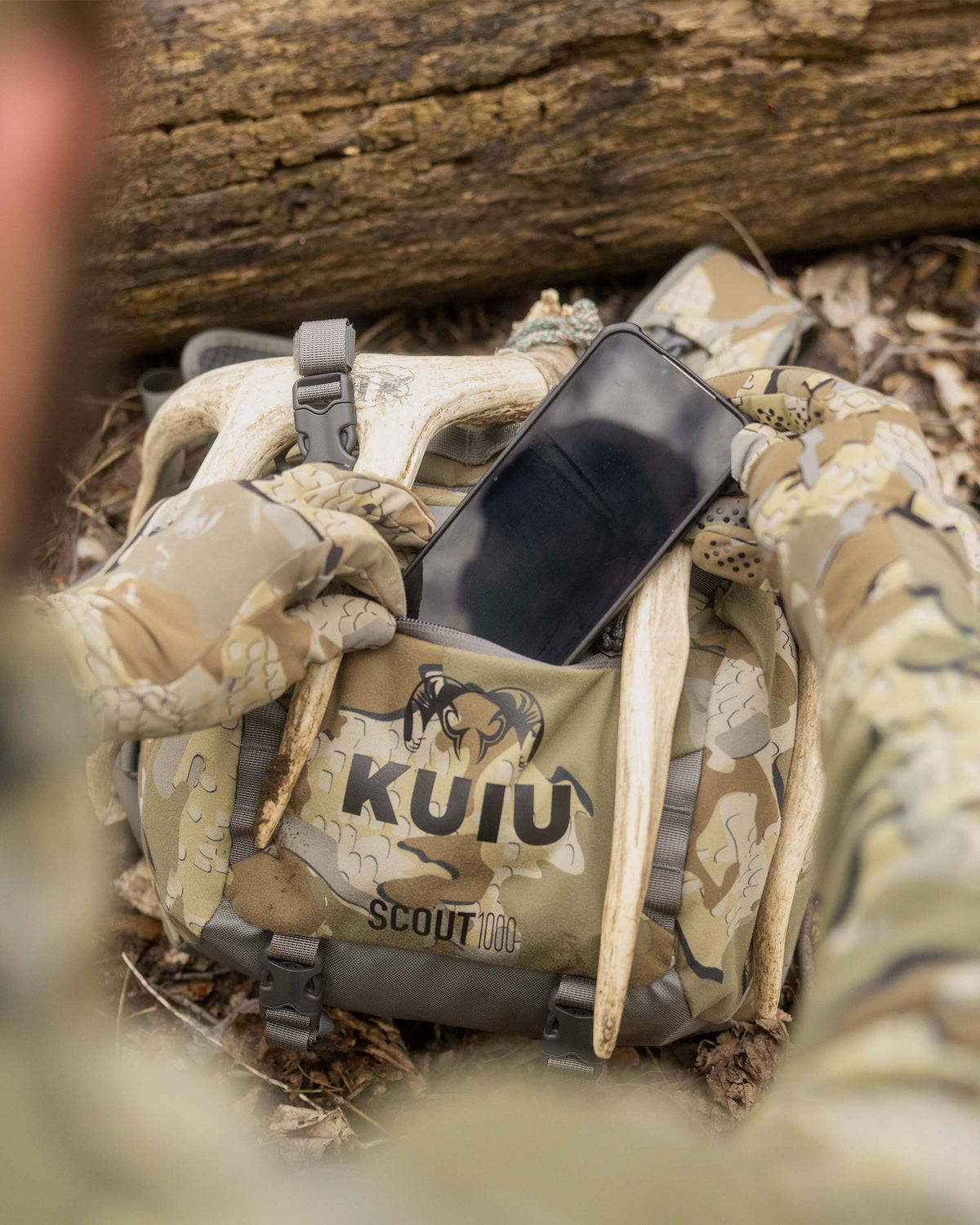 Close-up shot of Whitetail hunter stowing a cell phone in front zippered pocket of Scout 1000 in Valo Camouflage