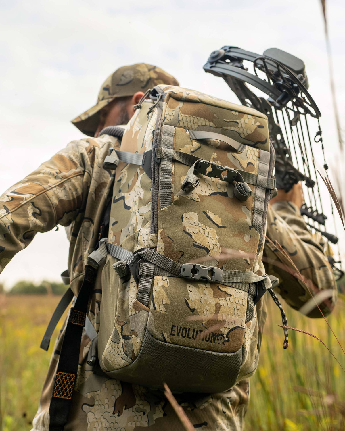 Close-up, back view of Whitetail hunter carrying Evolution 1800 on his back holding a compound bow in his right hand