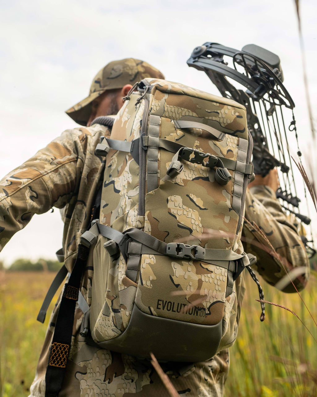 Close-up, back view of Whitetail hunter carrying Evolution 1800 on his back holding a compound bow in his right hand