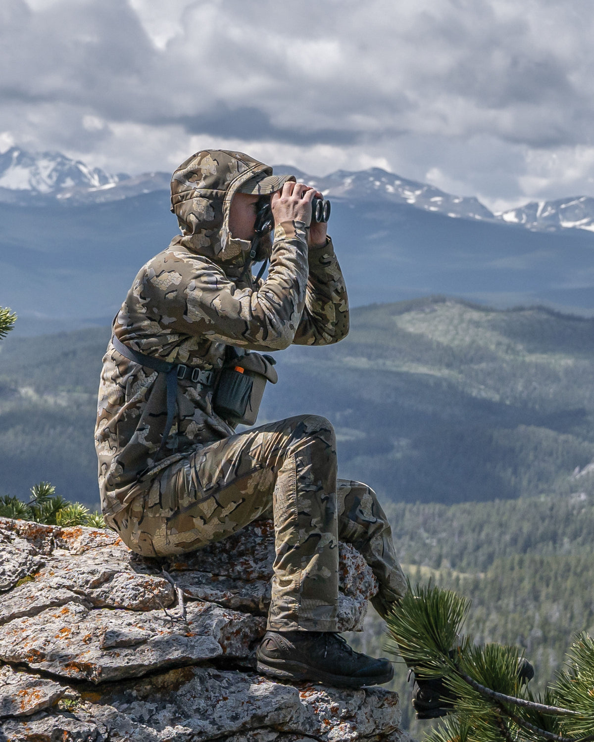Hunter seated on rock, glassing from a binoculars wearing StrongFleece 275 Full Zip Hoodie in Valo Camouflage