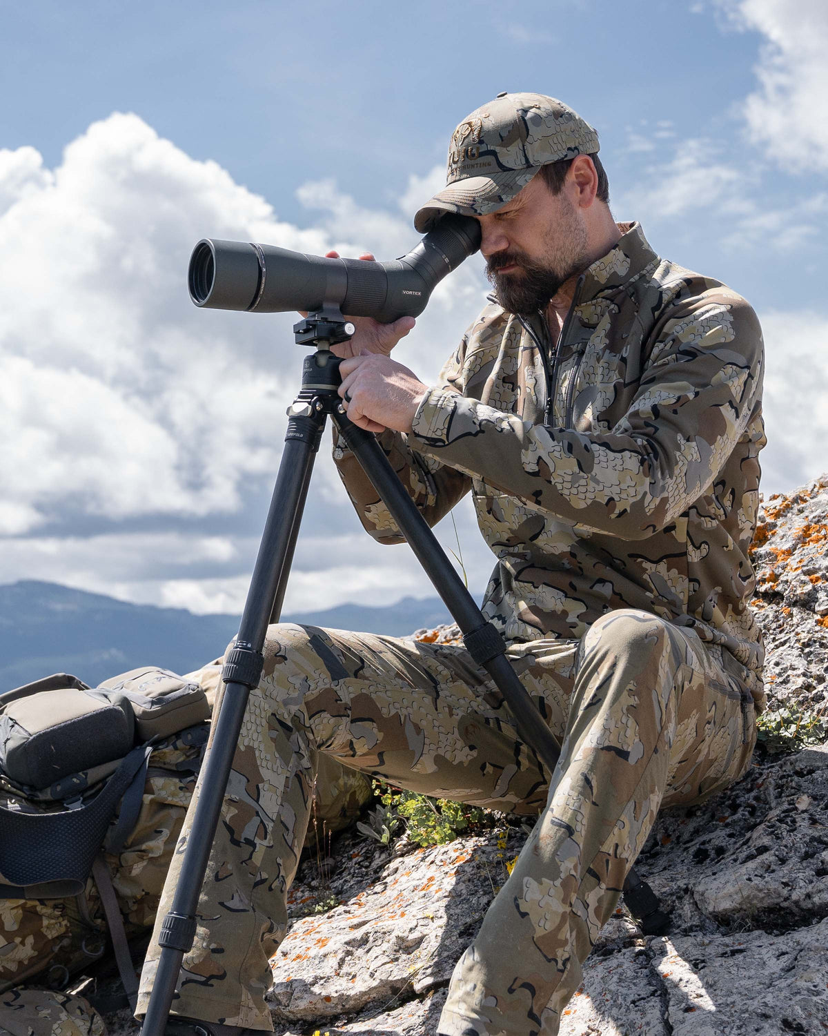 Hunter seated on rock, glassing from spotter wearing StrongFleece 1920 Zip-T in Valo Camouflage