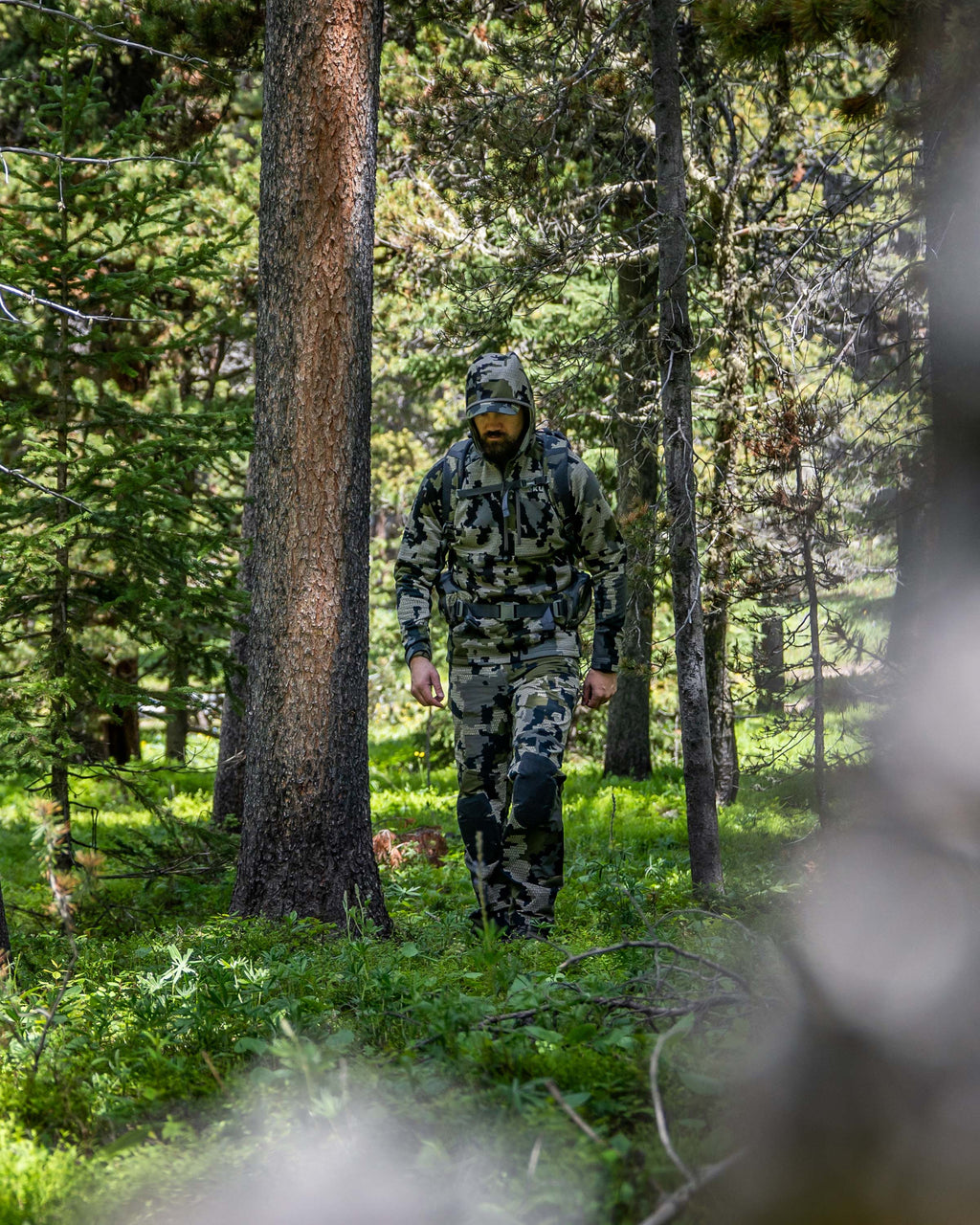 Hunter walking in forested area wearing StrongFleece 235 Zip-T Hoodie in Verde Camouflage