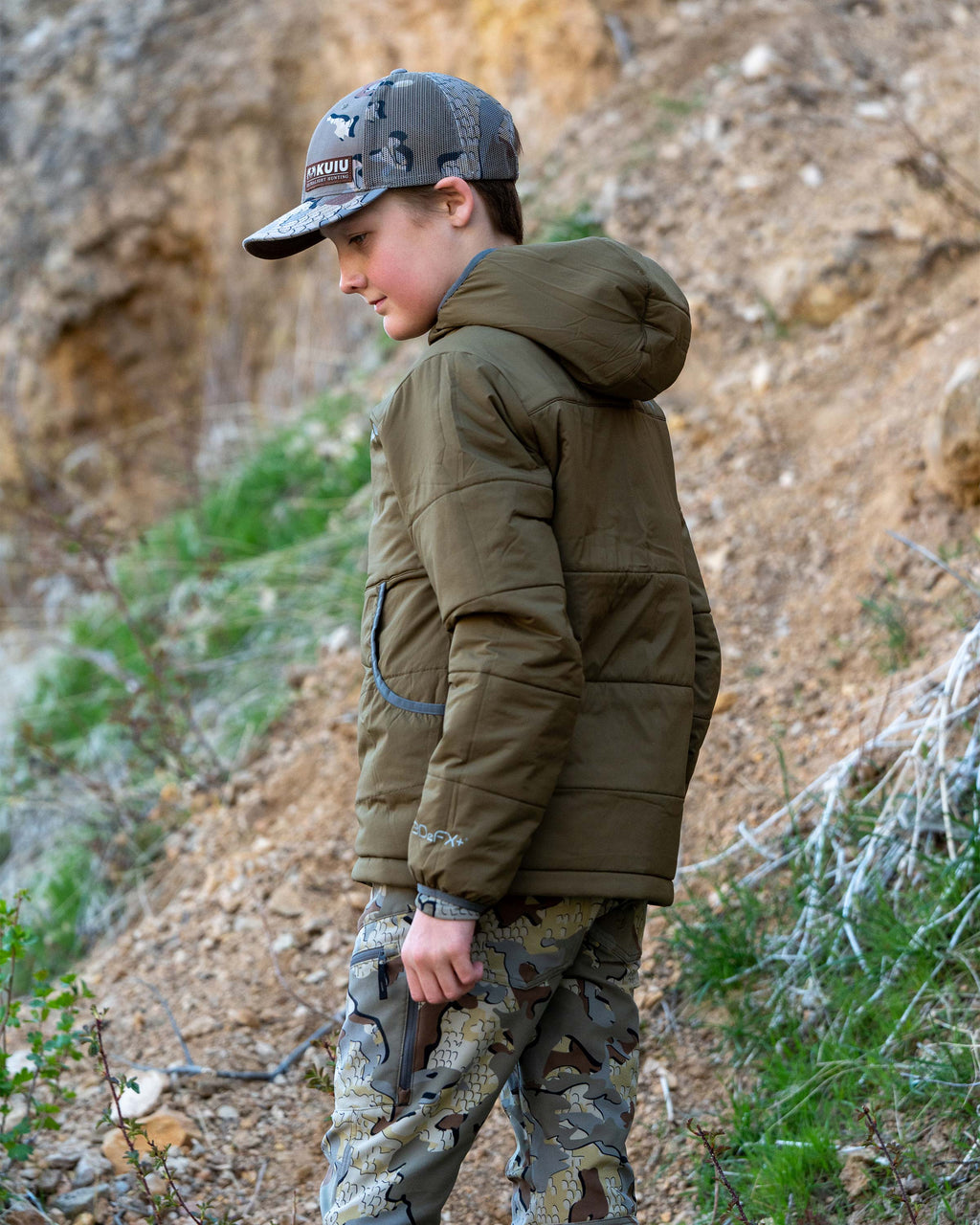 Side view of youth wearing the reversible side in Bourbon Brown color of the Youth Reversible Versa Jacket in Valo Camouflage