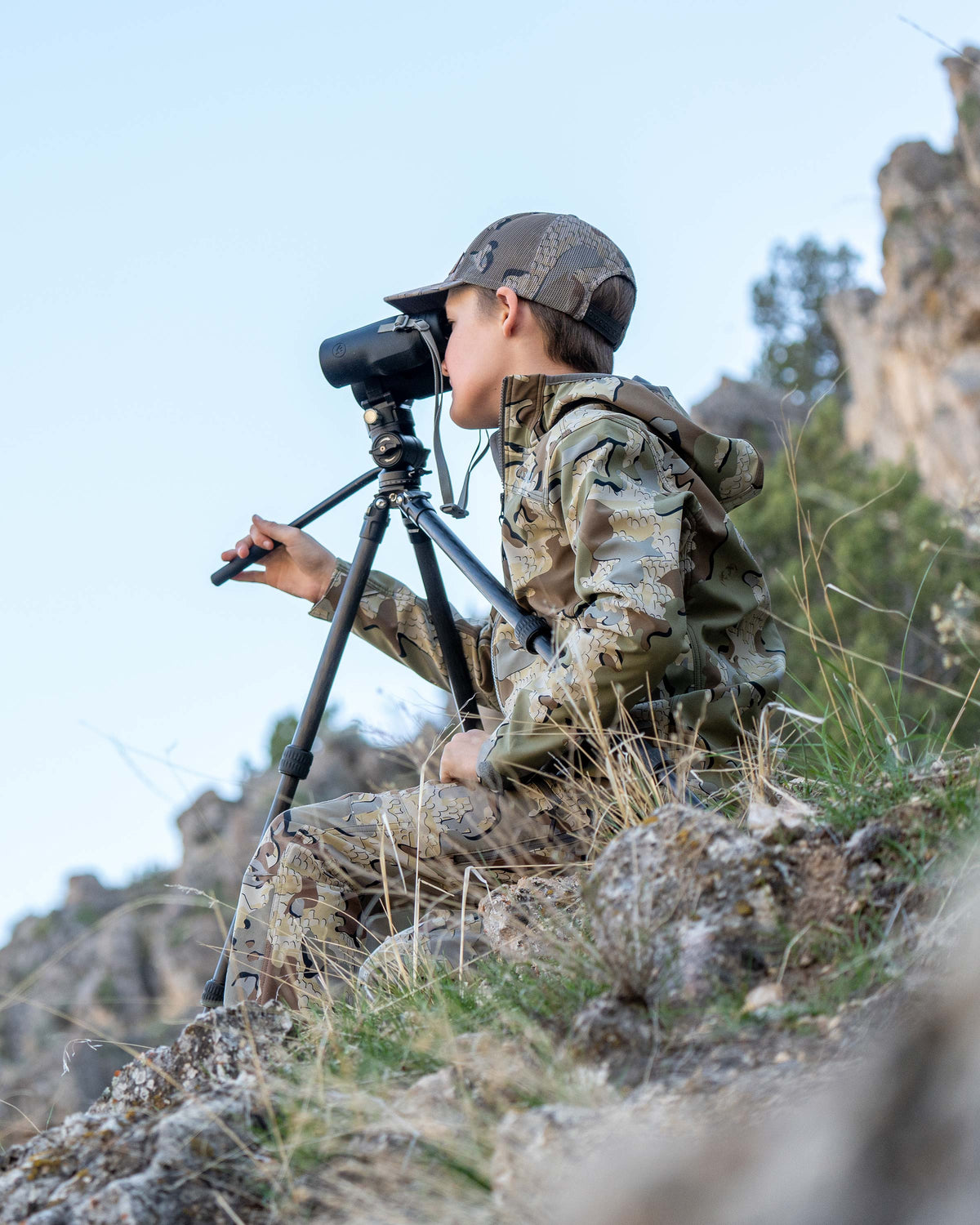 Youth glassing on a high vantage point wearing Youth Trailblazer Jacket in Valo Camouflage