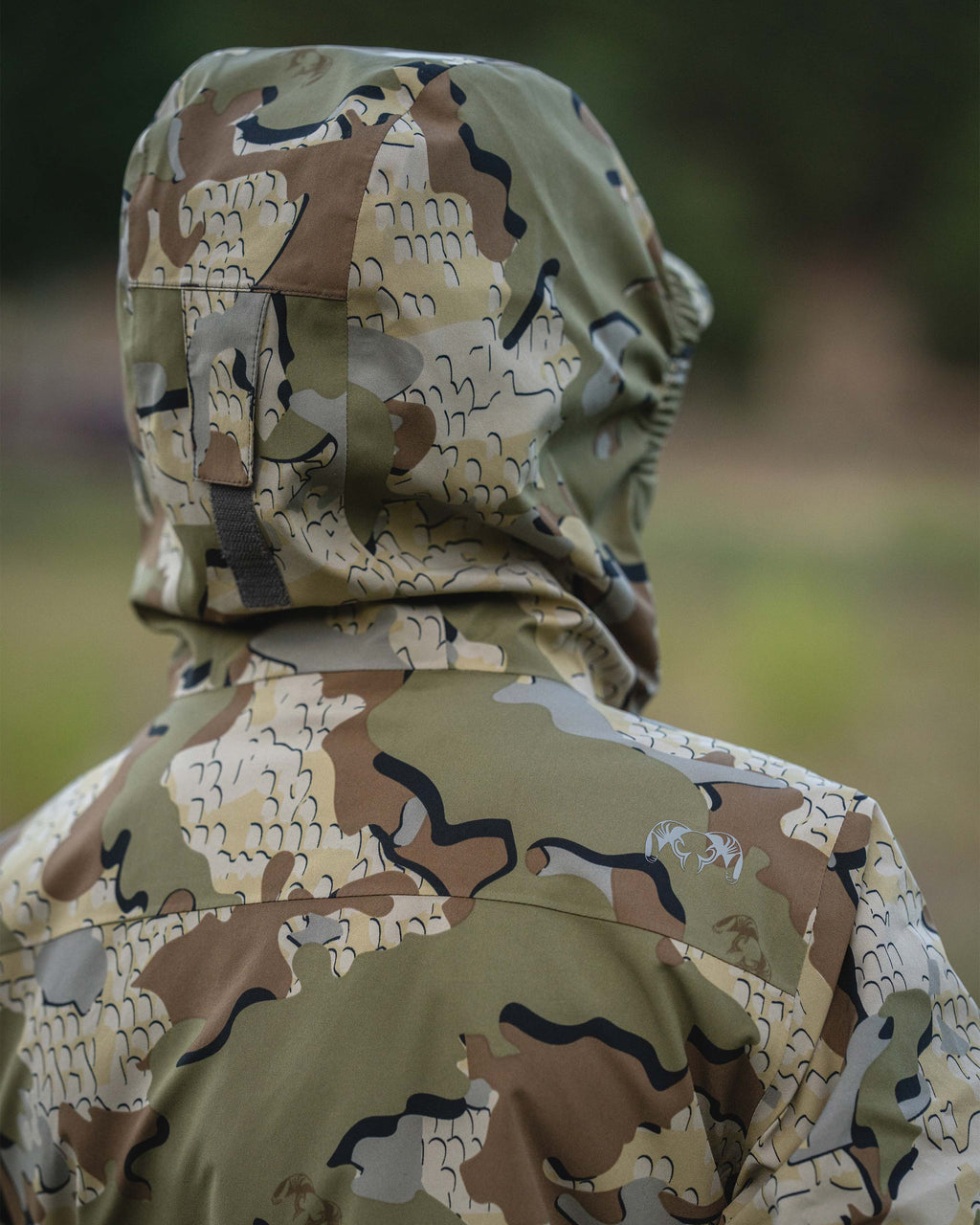 View from behind of a young male teenager wearing a hooded Youth Versa Jacket in Valo camouflage jacket in an outdoor setting.