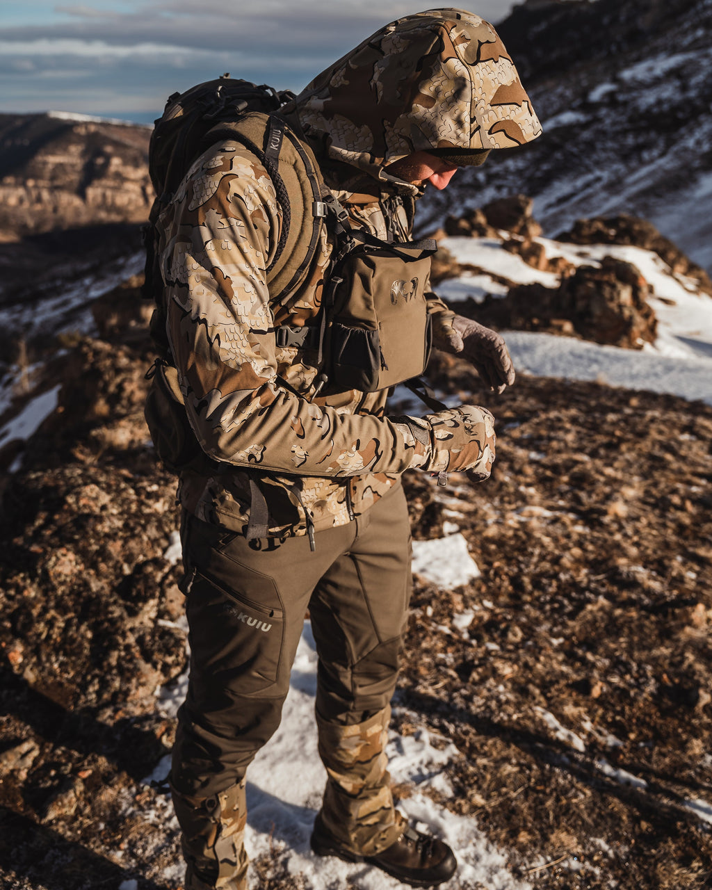 Hunter tightening his waist belt of a backpack while wearing the Axis Hybrid Hooded Jacket in Valo Camouflage
