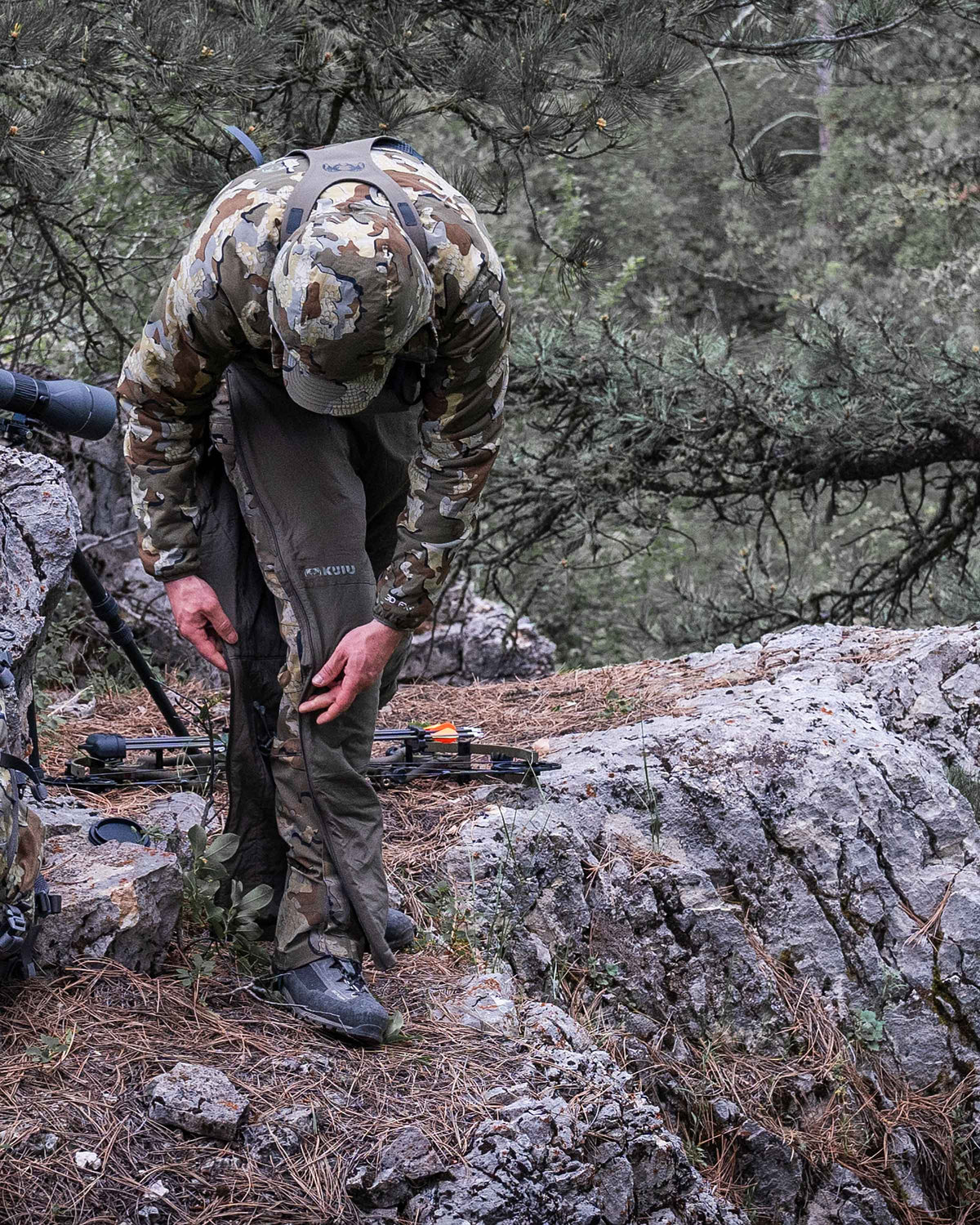 Hunter in field putting on Kenai Pant in Ash Brown