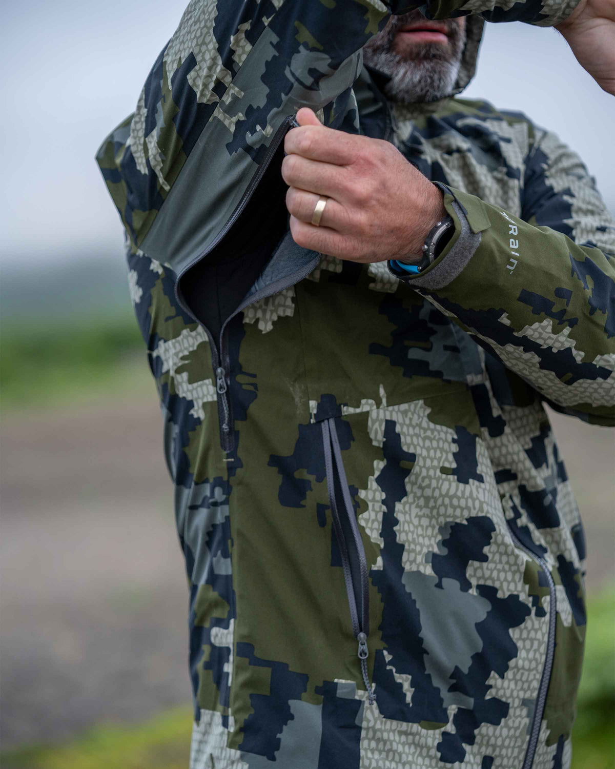 Hunter showing use of pit zips on Chugach TR Rain Jacket in Verde Camouflage