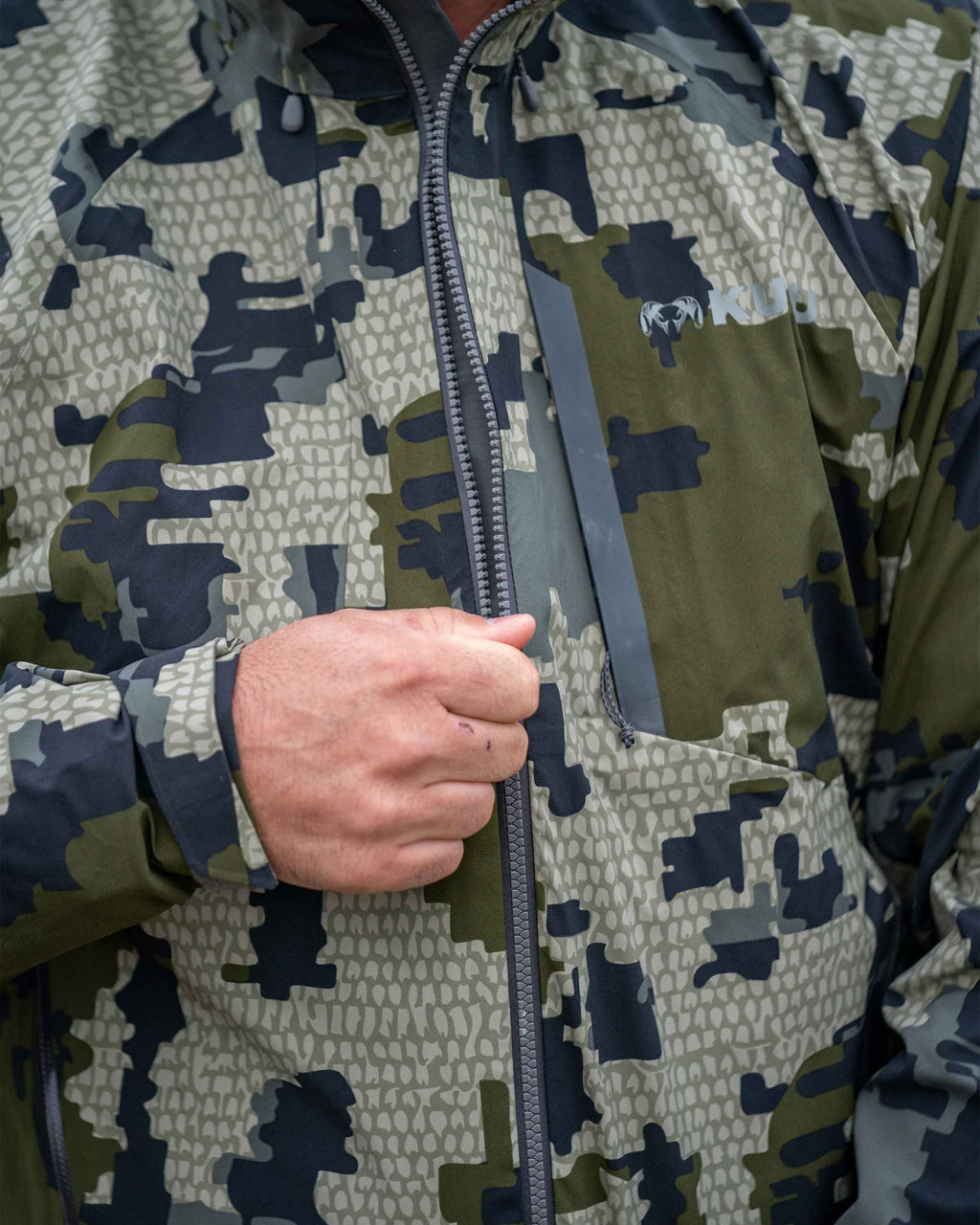 Hunter Zipping Up Chugach TR Rain Jacket in Verde Camouflage Highlighting YKK Aquaguard Zippers and Chest pocket