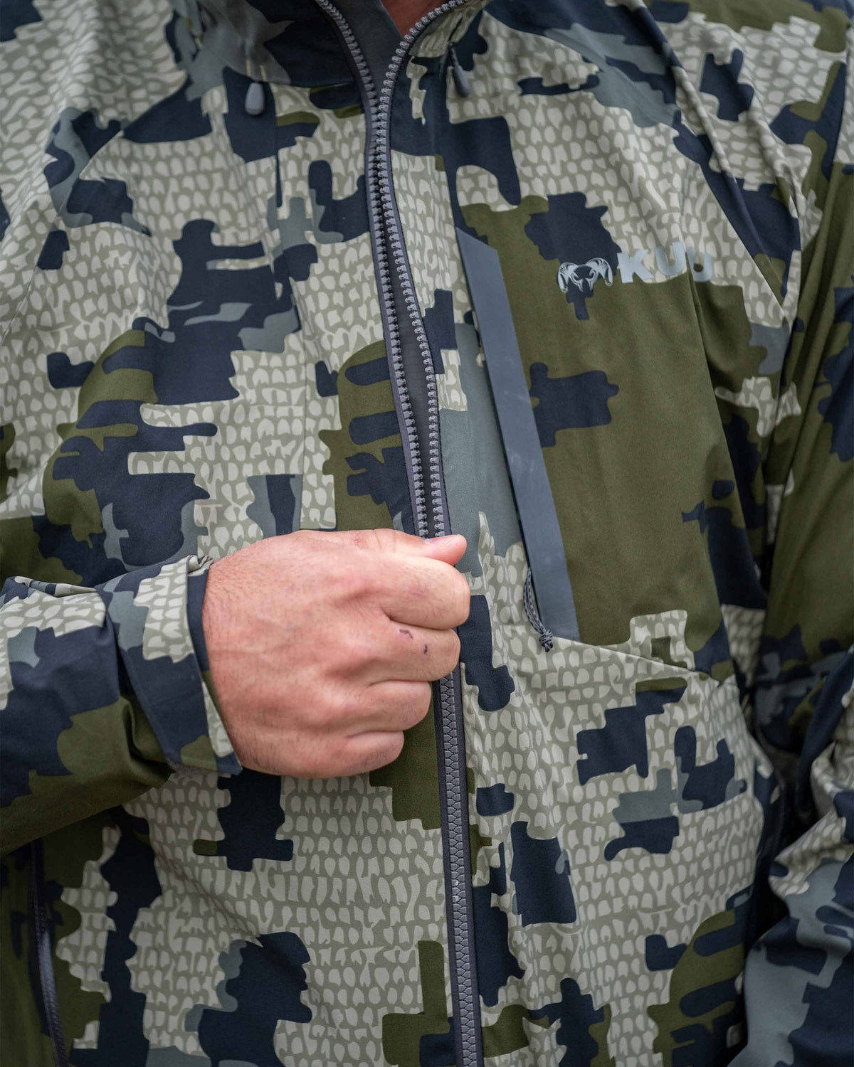 Hunter Zipping Up Chugach TR Rain Jacket in Verde Camouflage Highlighting YKK Aquaguard Zippers and Chest pocket