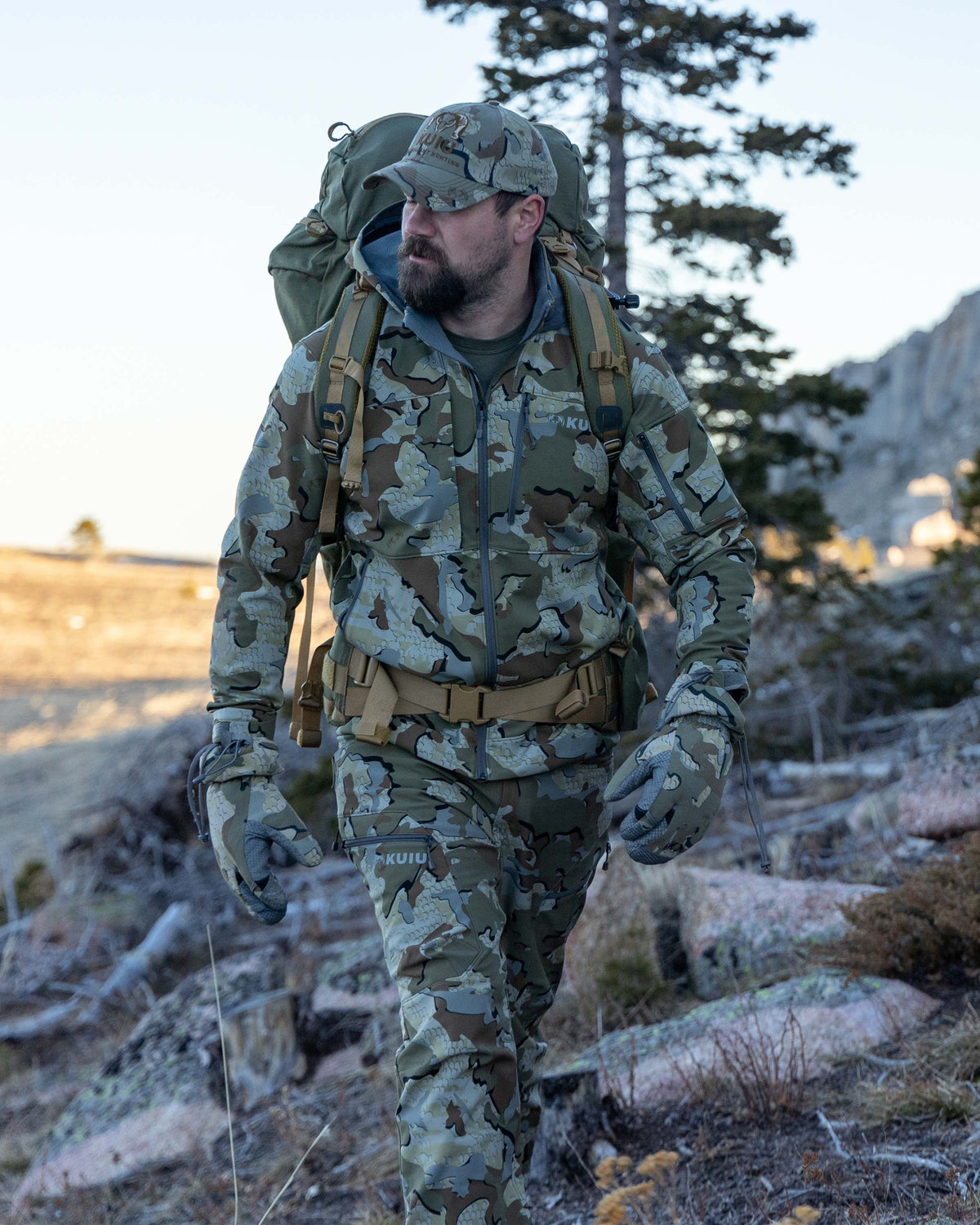 Hunter Wearing Pack Walking Through Open, Dry Country Wearing Guide PRO Hooded Jacket in Valo Camouflage
