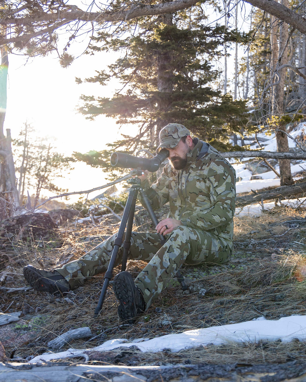 Hunter Looking Through Spotting Scope on Partially, Snow Covered Hillside Wearing Guide PRO Hooded Jacket in Valo Camouflage