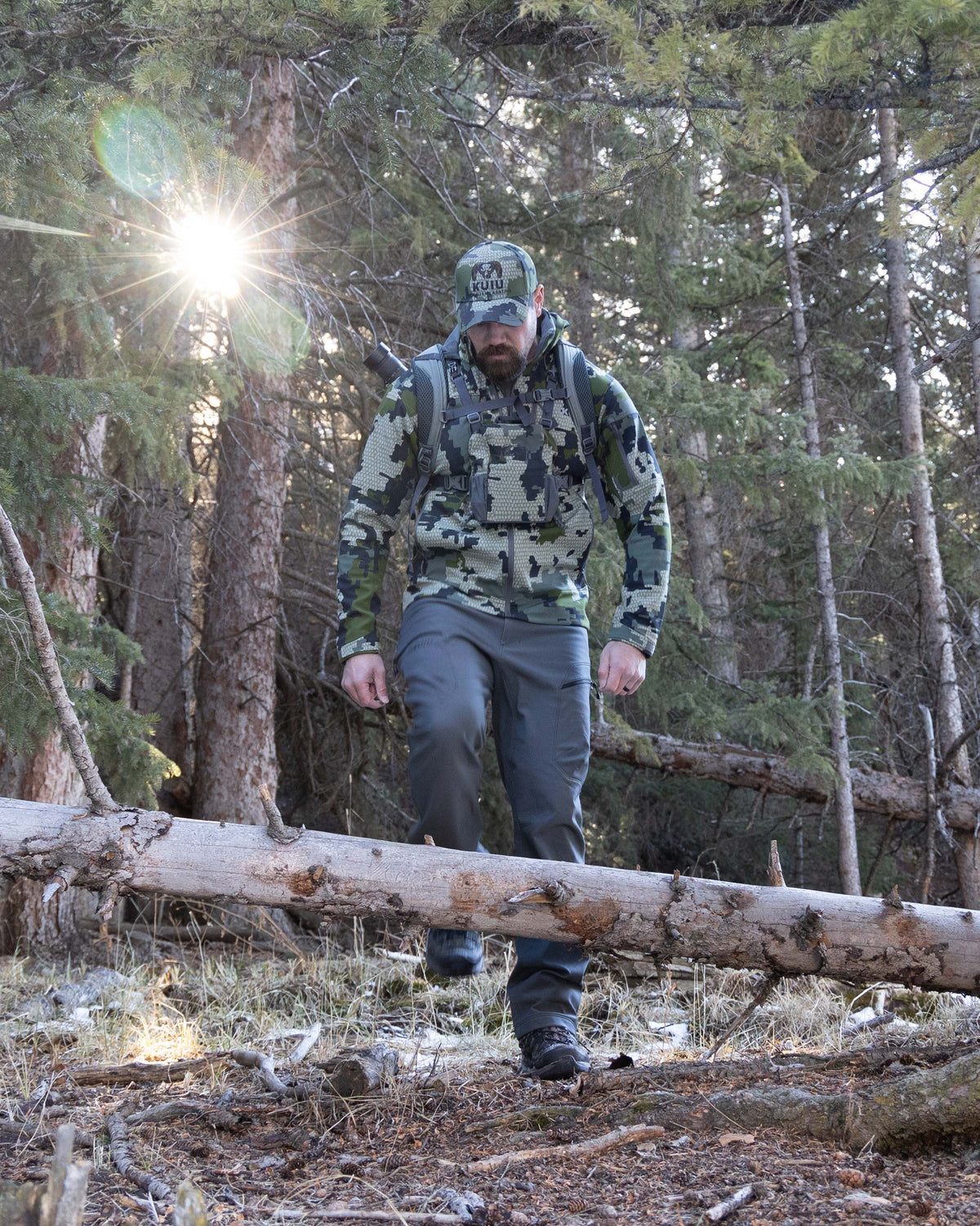Hunter Walking Through Pine Forest with One Leg Raised Wearing Guide PRO Pants in Gunmetal Grey