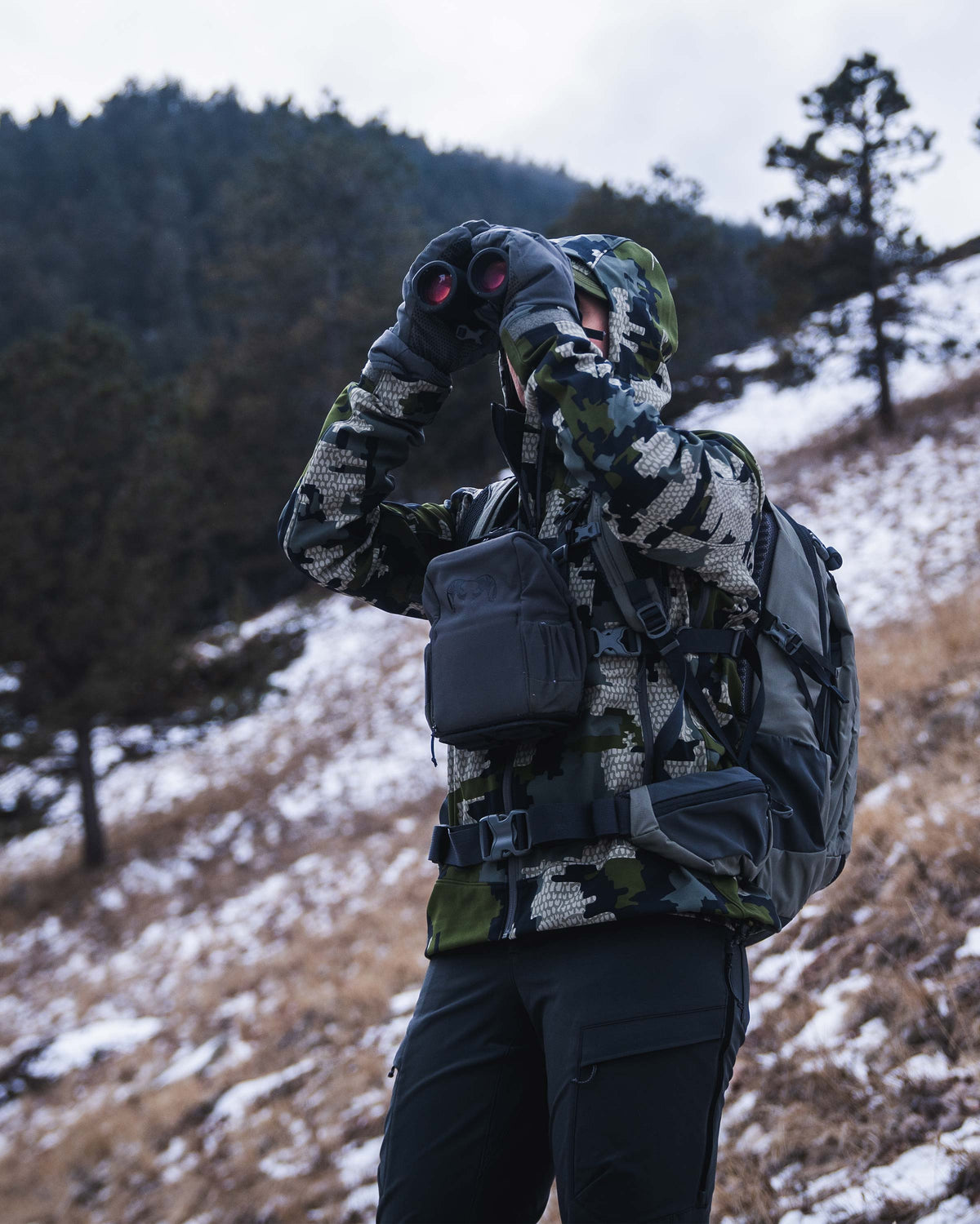 Front quartering-to view of  female hunter wearing Women's Guide PRO Hooded Jacket in Verde camouflage while looking through binoculars