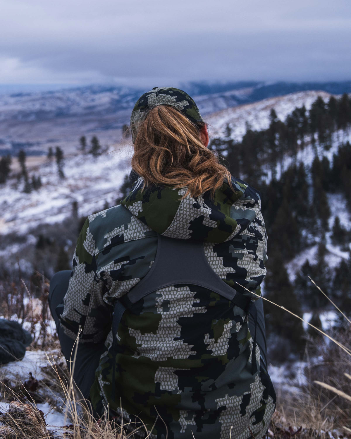 Rear view of seated female hunter wearing Women's Guide PRO Hooded Jacket in Verde camouflage
