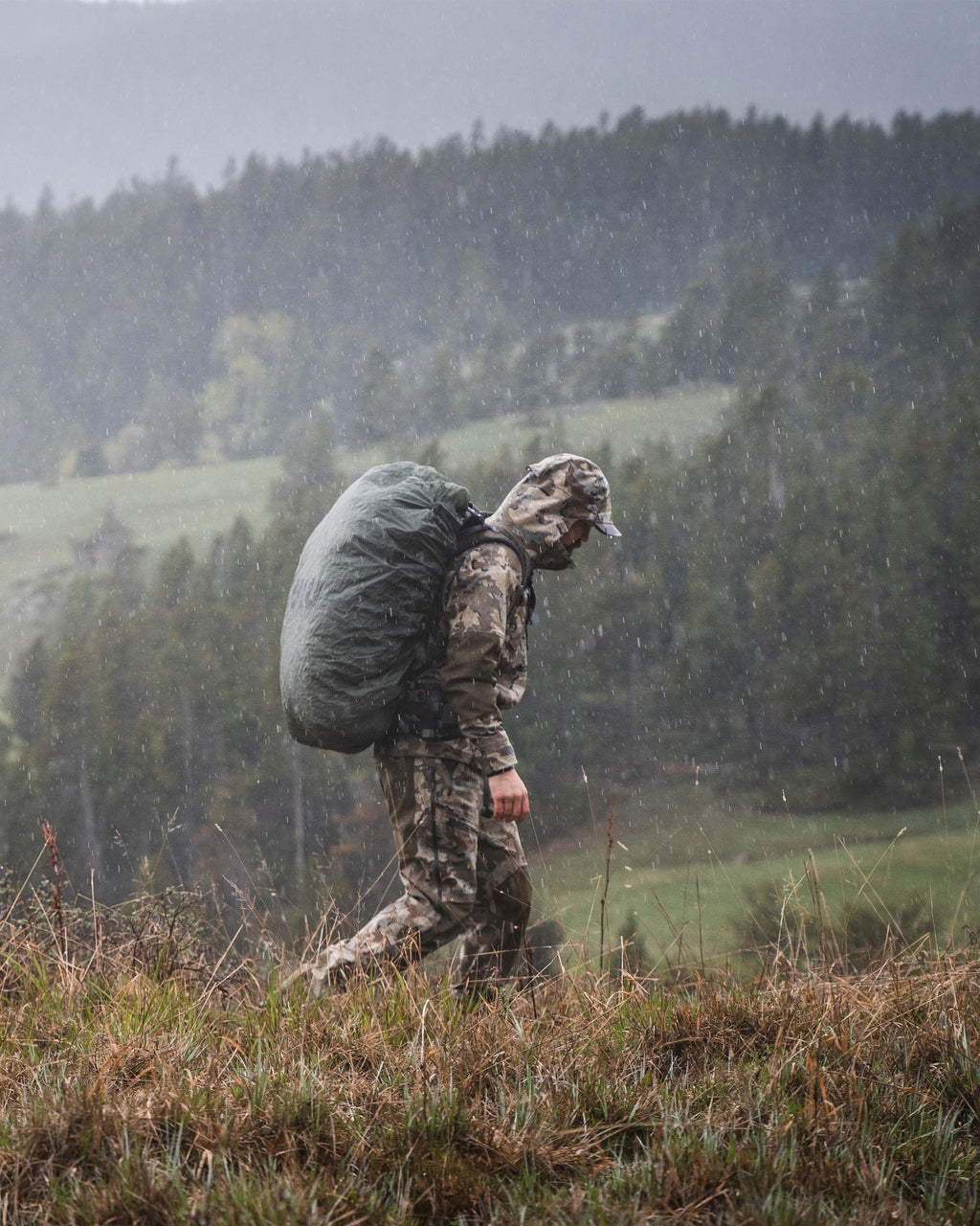 Side profile view of hunter wearing Yukon TR Rain Jacket in Valo camouflage walking on top of a hill while wearing a backpack