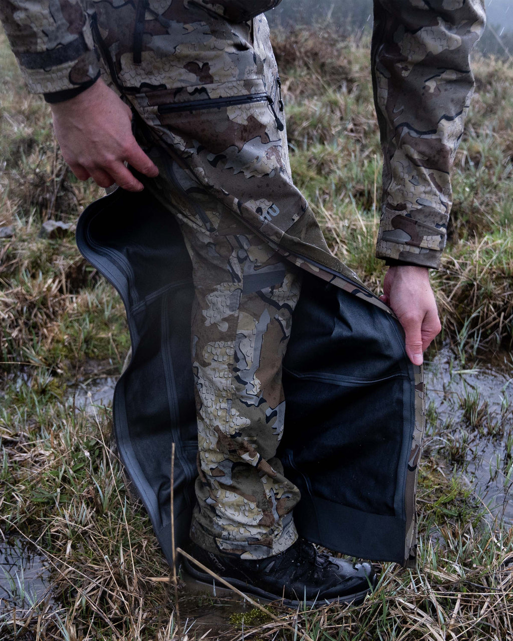 Hunter Exposing Interior of Yukon TR Rain Pants in Valo Camouflage Highlighting Full Length YKK Aquaguard Leg Zipper and Waterproof Torain Taped Seams