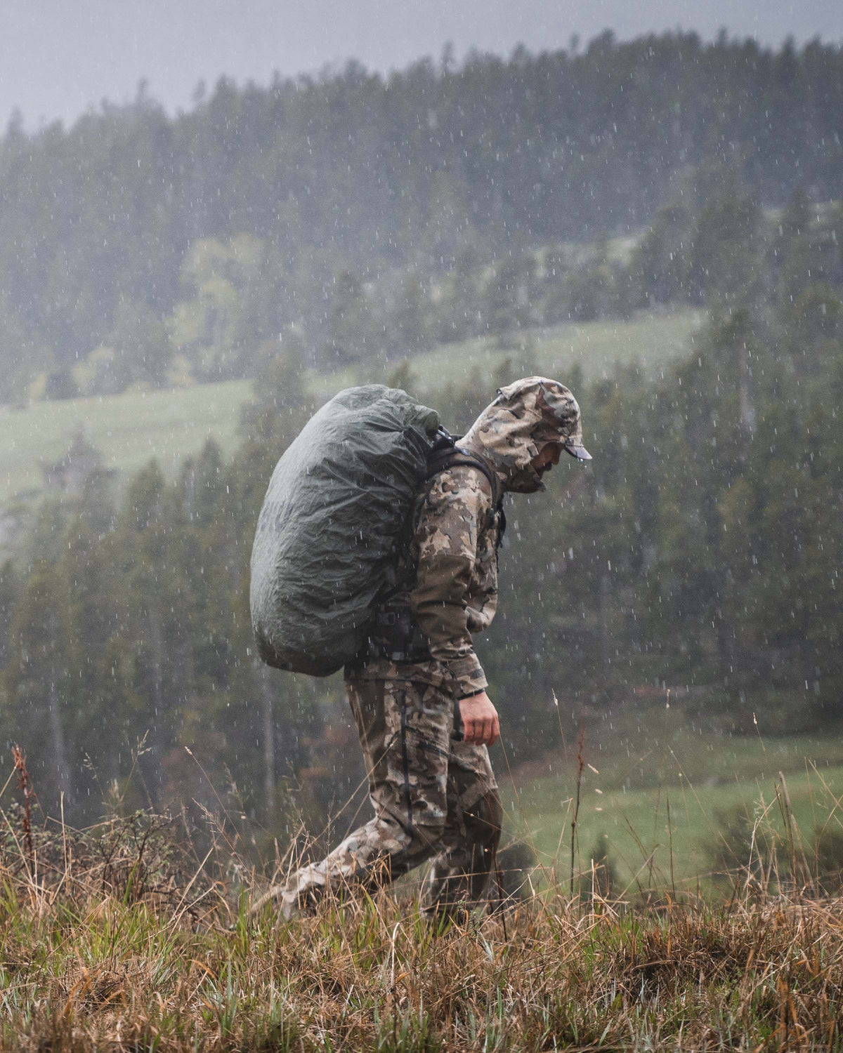 Hunter Walking on Grassy Ridge in the Rain Wearing Yukon TR Rain Pants in Valo Camouflage