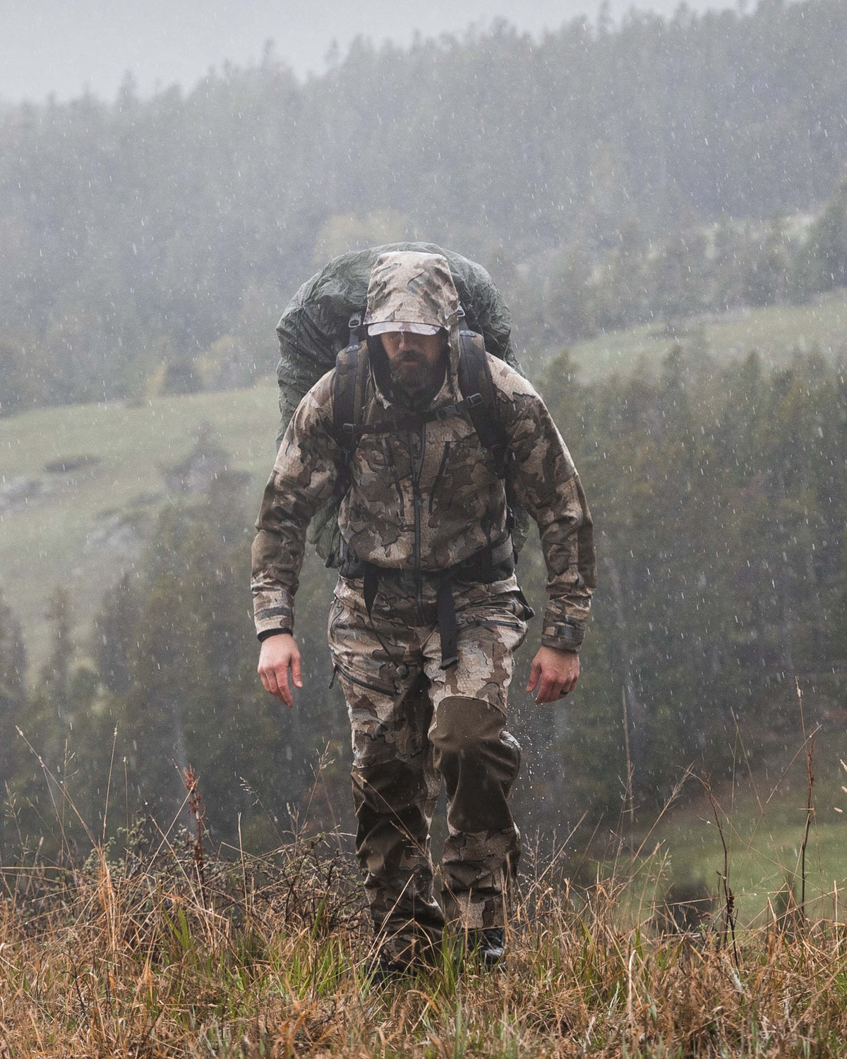 Front Profile of Hunter Walking on Grassy Ridge in the Rain Wearing Yukon TR Rain Pants in Valo Camouflage