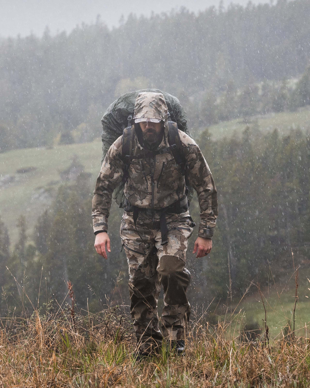 Front Profile of Hunter Walking on Grassy Ridge in the Rain Wearing Yukon TR Rain Pants in Valo Camouflage
