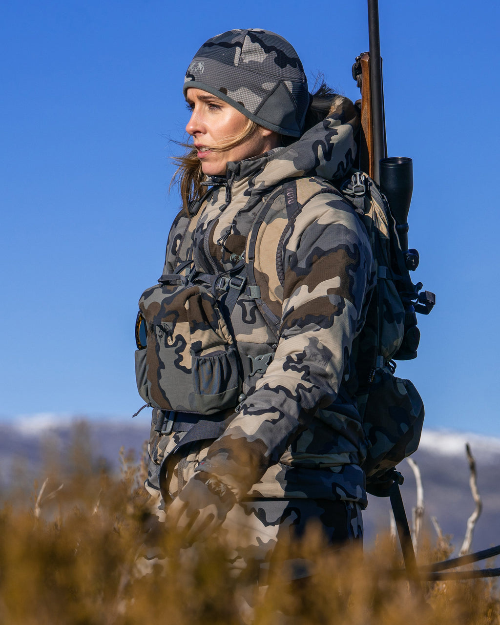 female hunter walking in tall brush wearing Women's Kenai Hooded Jacket in Vias Camouflage