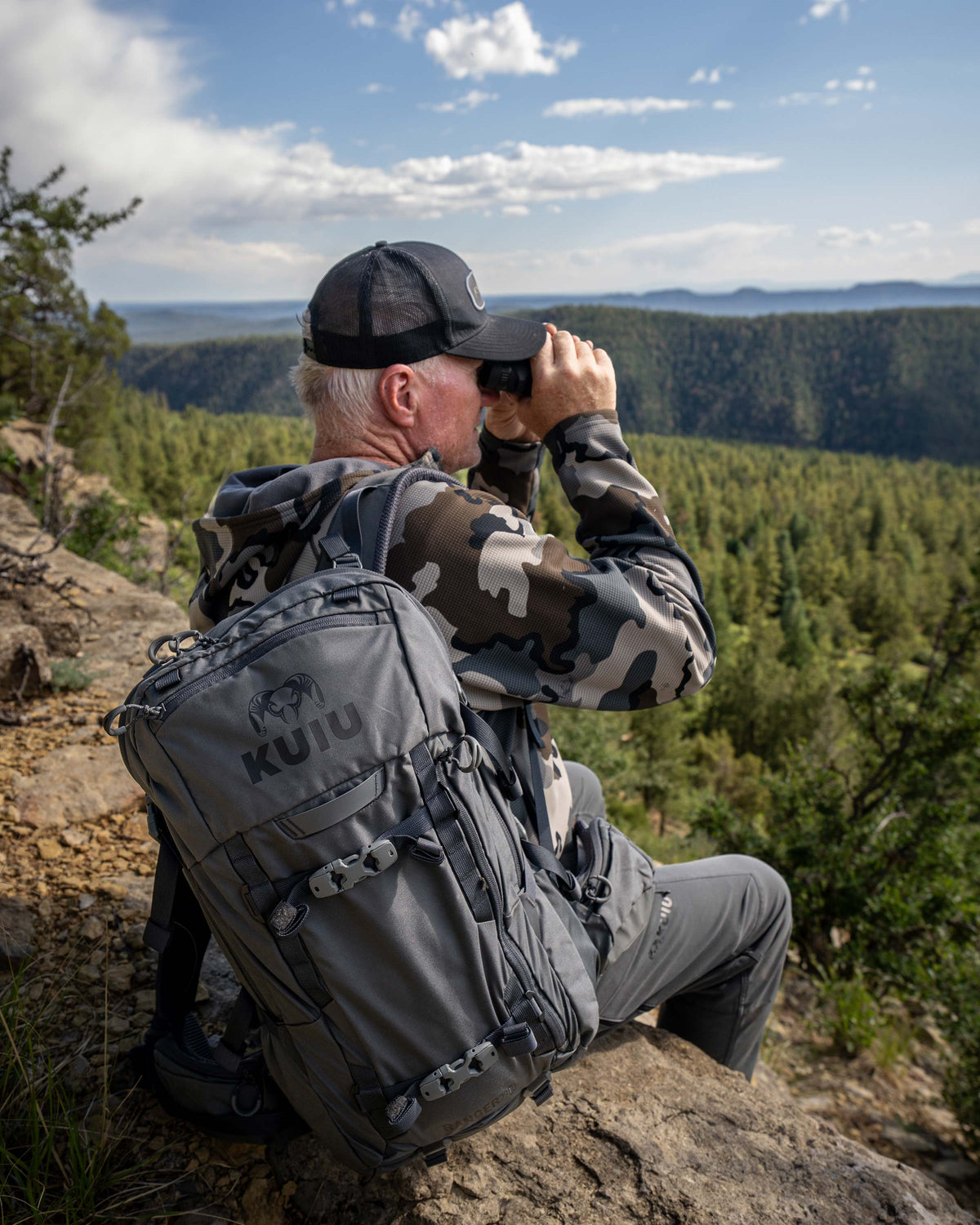 Hunter sitting on a rocky edge while glassing, carrying the Ranger 2200 in Gunmetal Grey on his right shoulder