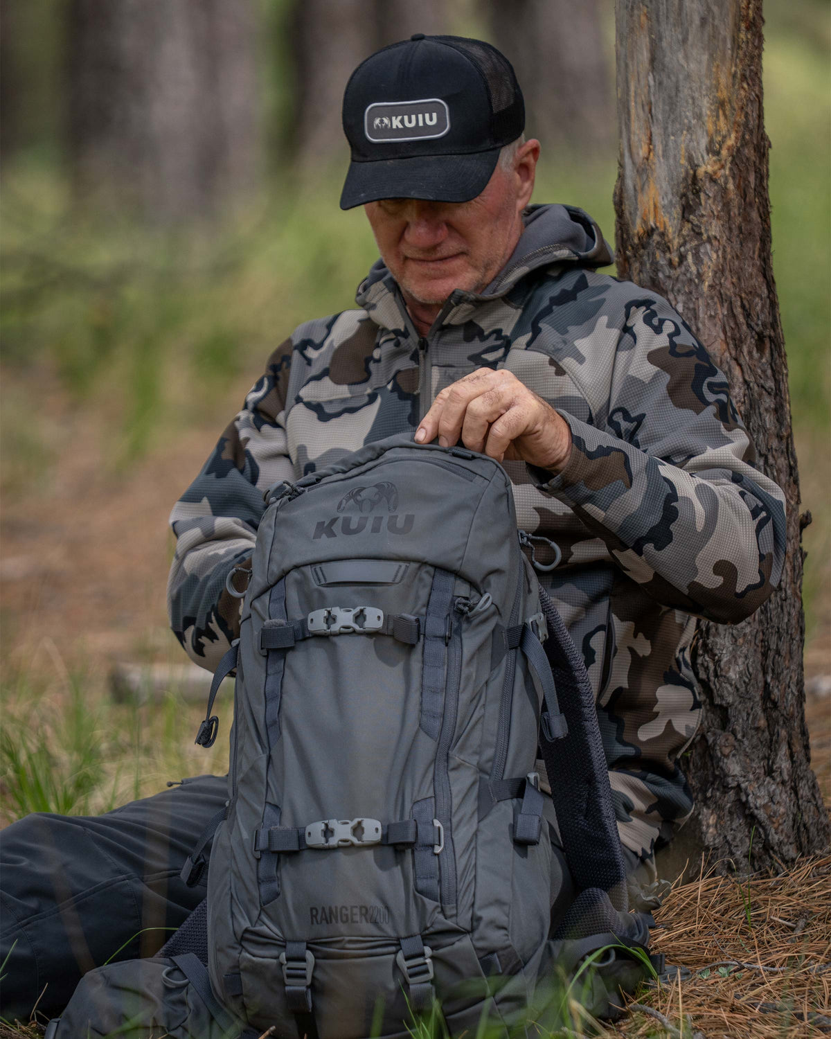 Hunter sitting down next to a tree looking inside Ranger 2200 in Gunmetal Grey