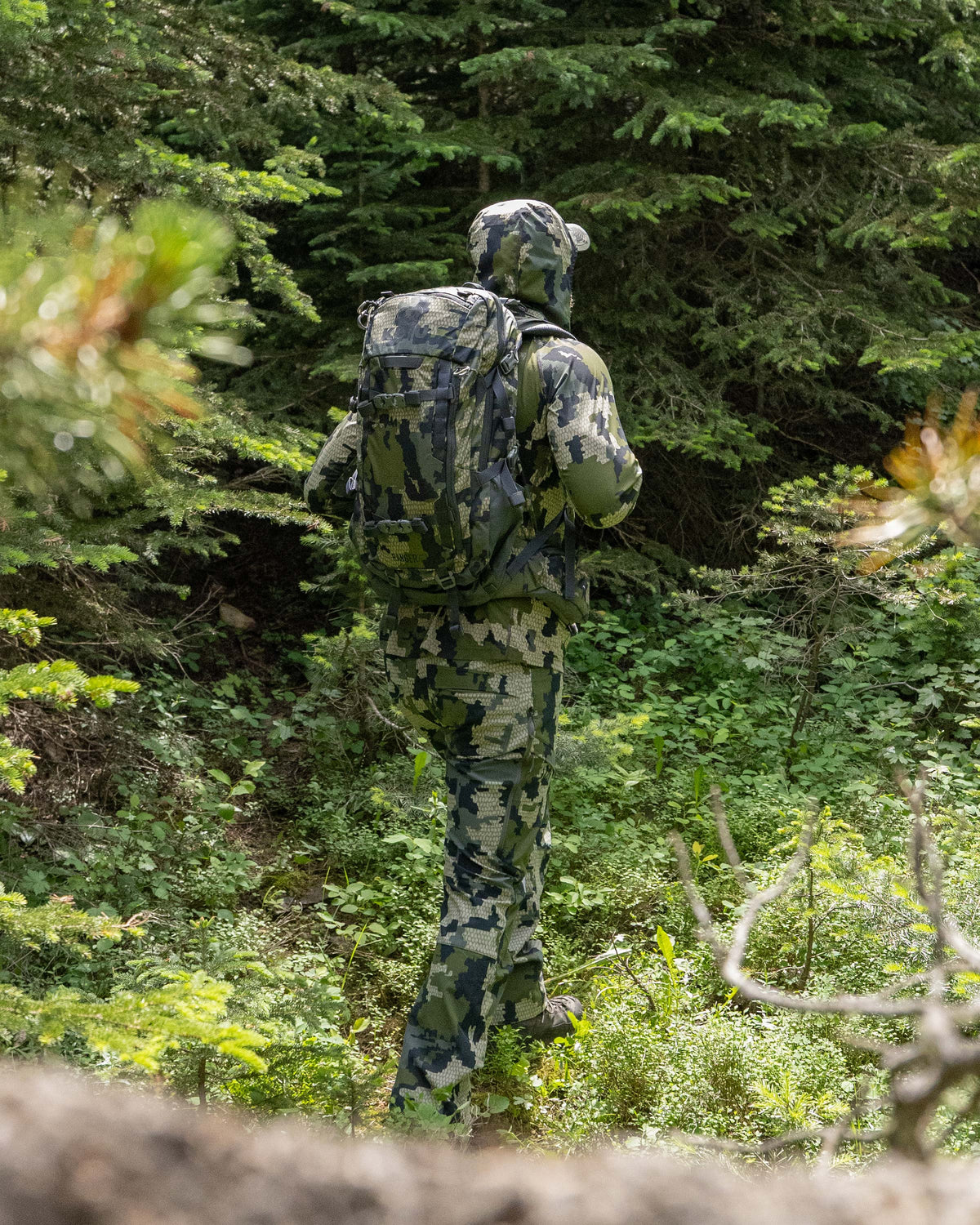 A camouflaged hunter in the middle of a green forest with the Ranger 2200 in Verde Camouflage on his back