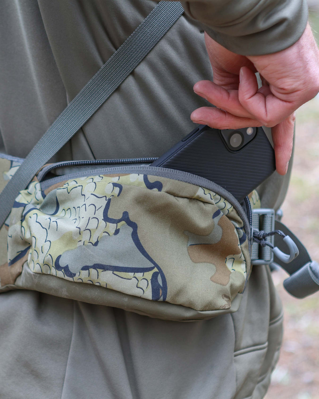 Close-up of hunter stowing a cell phone in the zippered pocket of the Ranger 2200 removable waist belt