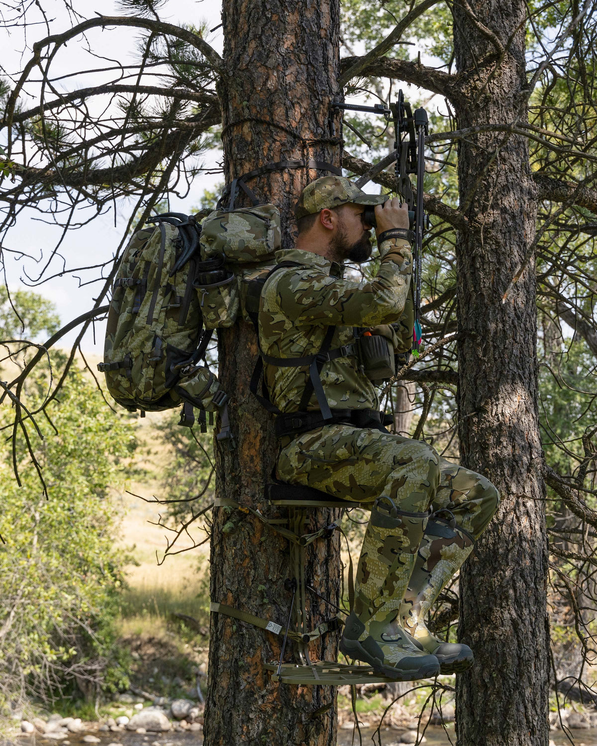 Hunter glassing, sitting in the treestand with the Encounter Divide 2800 in Valo Camouflage strapped on the tree