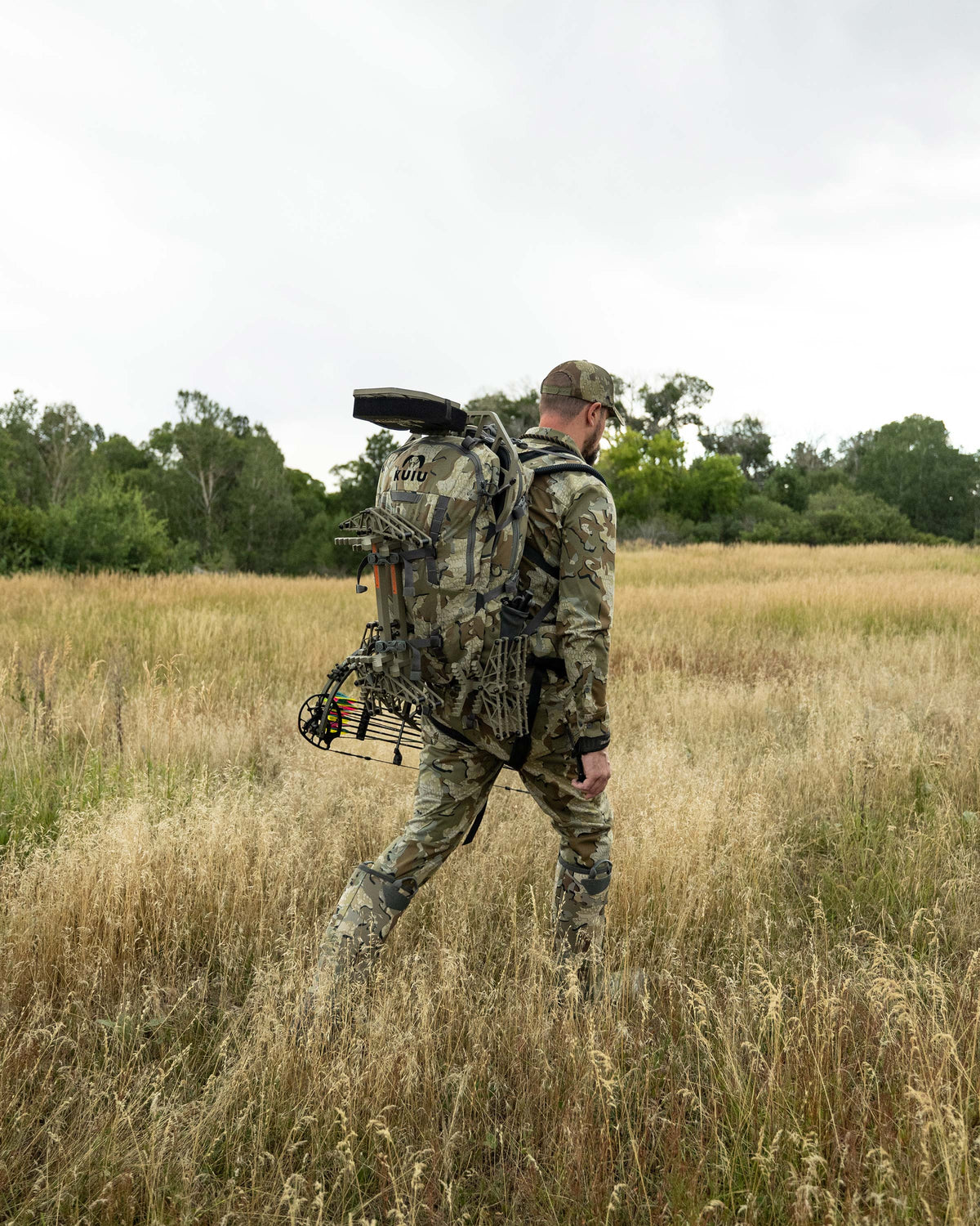Hunter backpacking through the meadow carrying the Encounter Divide 2800 in Valo Camouflage