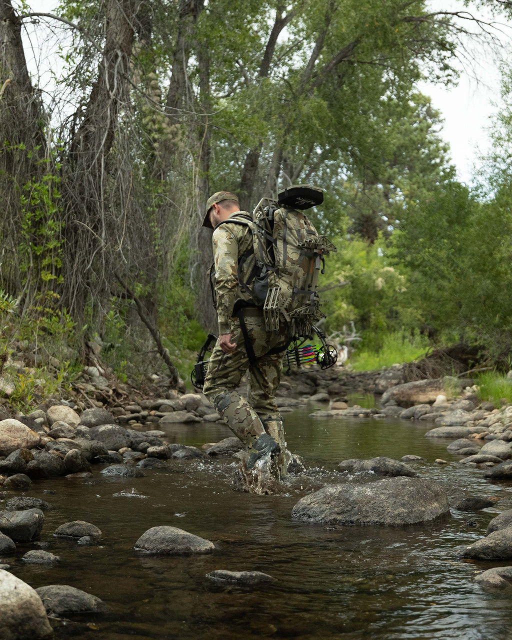 Hunter backpacking through a creek carrying the Encounter Divide 2800 in Valo Camouflage