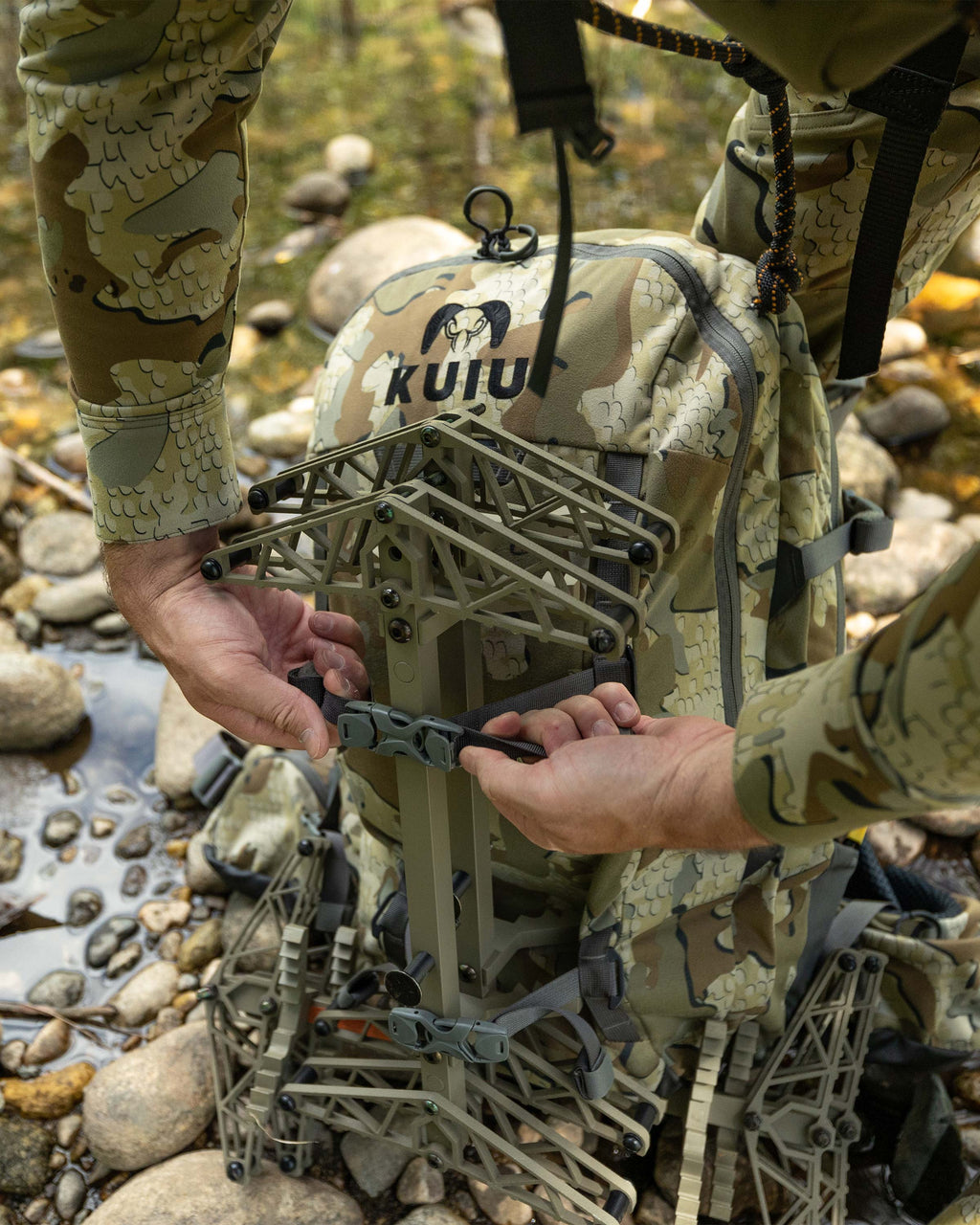 Close-up view of Hunter strapping a tree stand on the front exterior of the Encounter Divide 2800 in Valo Camouflage using compression straps