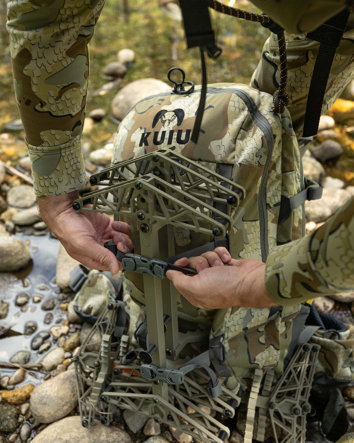 Close-up view of Hunter strapping a tree stand on the front exterior of the Encounter Divide 2800 in Valo Camouflage using compression straps