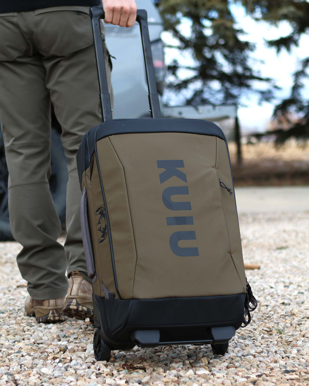 Man pulling Waypoint 3000 Carry-On Roller in Bourbon Brown over rough gravel