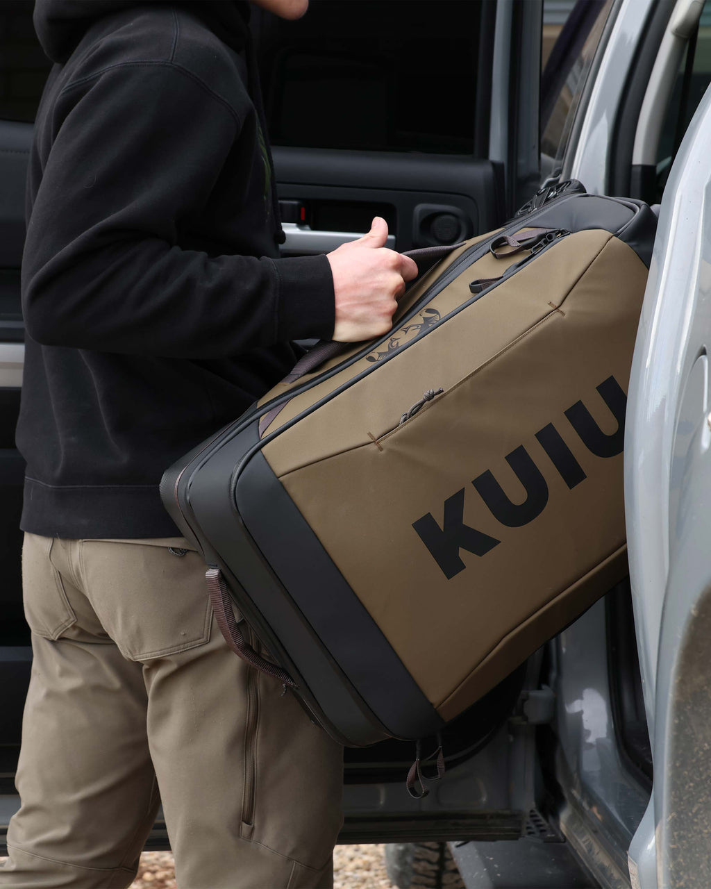 Man loading Waypoint 3000 Carry-On Roller in Bourbon Brown onto the rear passenger seat of a pickup truck