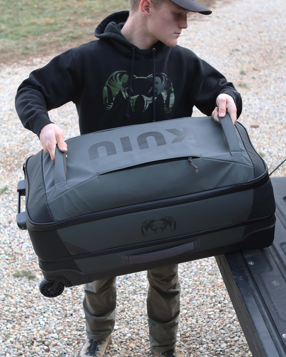 Person using front grab handles to load Waypoint 3000 Carry-On Roller in Gunmetal Grey onto the back cargo of a pickup truck