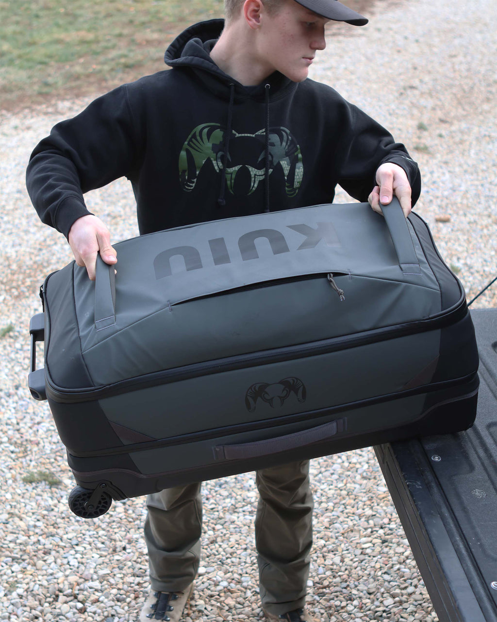 Person using front grab handles to load Waypoint 3000 Carry-On Roller in Gunmetal Grey onto the back cargo of a pickup truck