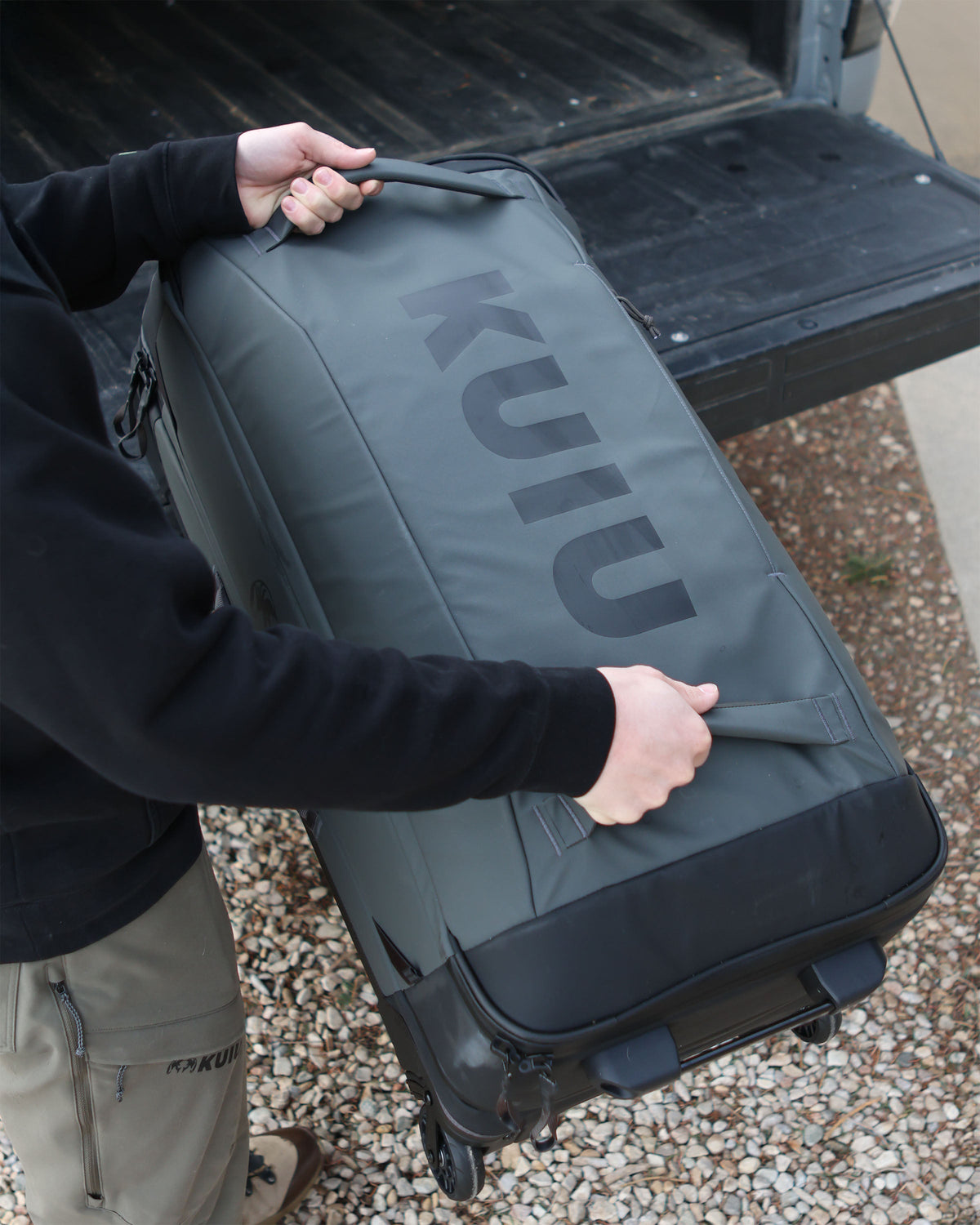 Person using front grab handles to load Waypoint 3000 Carry-On Roller in Gunmetal Grey onto the back cargo of a pickup truck