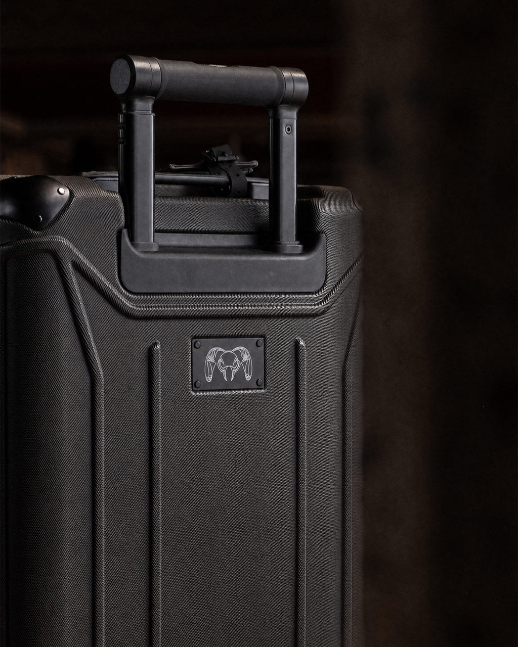 A close-up of the back Hardline Spinner Carry-On in Black with a telescoping handle and a small ram-head logo plaque located below the handle.