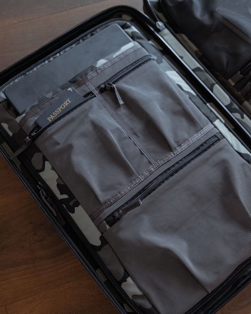 A gray fabric luggage organizer pouch with zippered pockets, neatly packed inside an open Hardline Spinner Carry-On on a wooden surface.