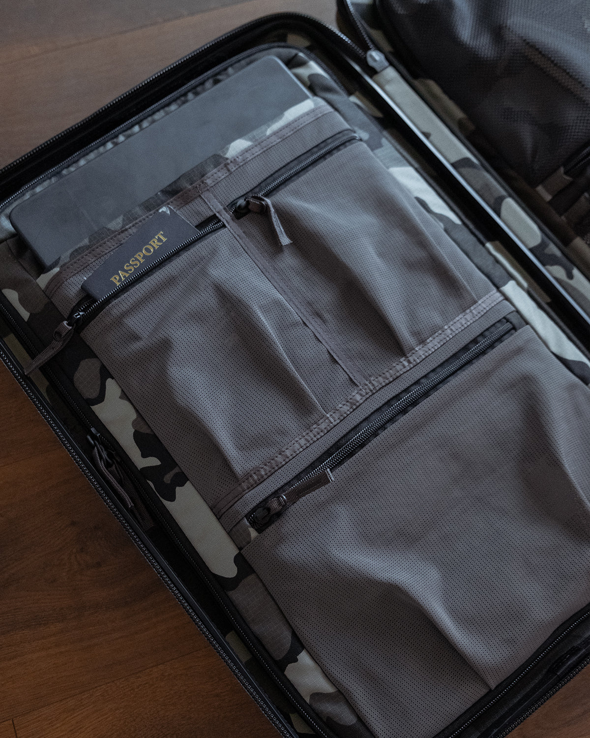 A gray fabric luggage organizer pouch with zippered pockets, neatly packed inside an open Hardline Spinner Carry-On on a wooden surface.