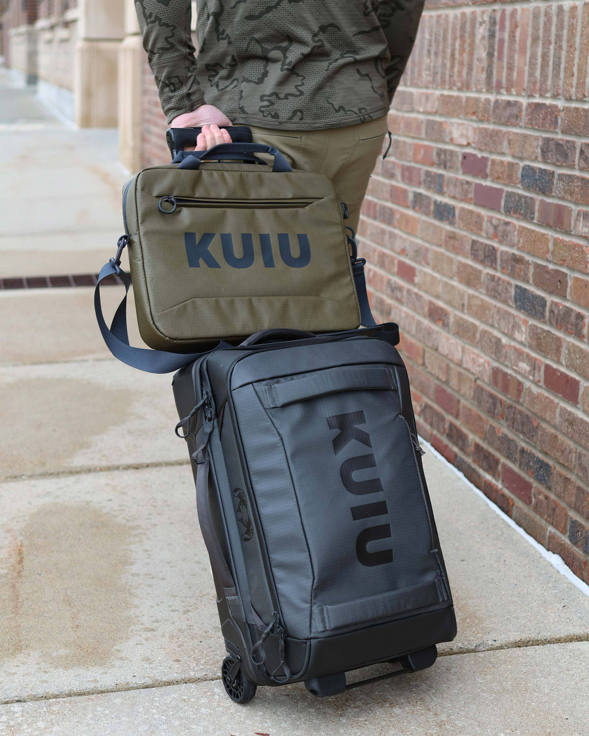 Man wheeling Waypoint 3000 Carry-On Roller in Gunmetal Grey with Waypoint Messenger Bag in Bourbon Brown securely placed over luggage handle