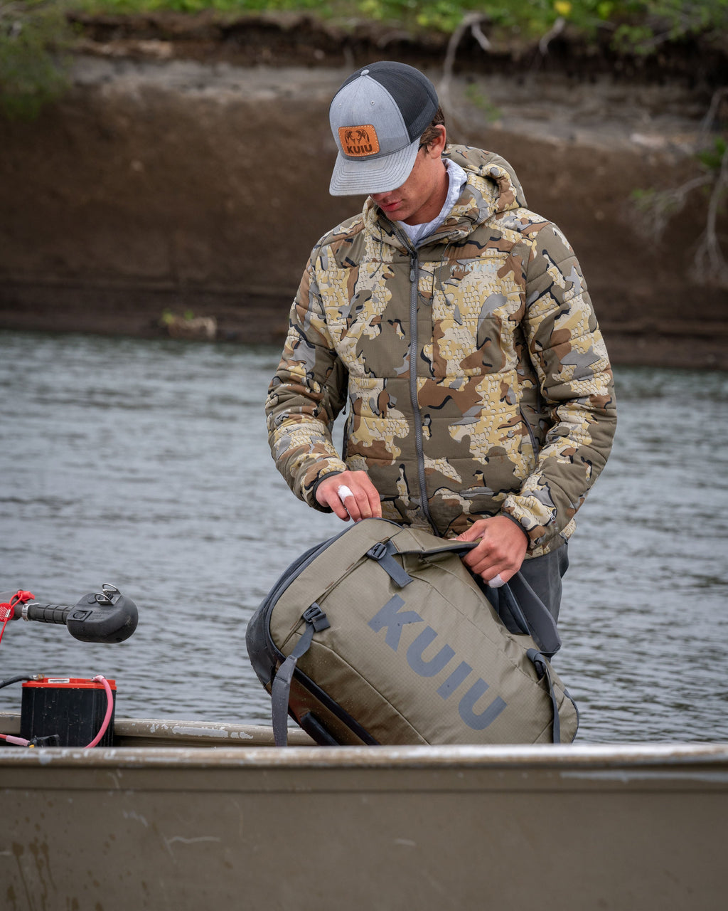 Picture of hunter in Valo Camouflage jacket unzipping a Bourbon Brown Waypoint 2800 Duffel Bag while standing in a boat