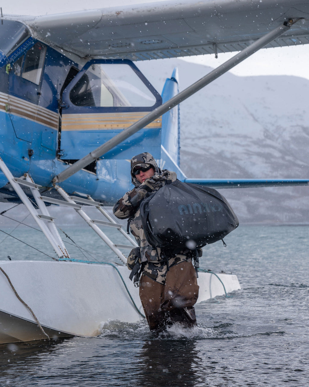 Picture of hunter carrying a black Waypoint 10400 Duffel bag from a float plane as he wades to the shoreline