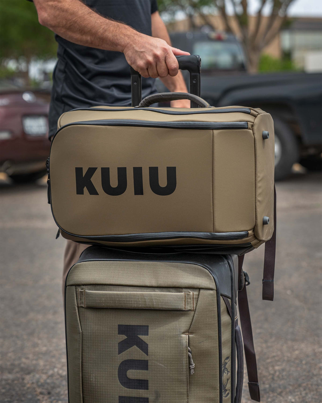 Person displaying Waypoint Travel Backpack stacked on Waypoint 4500 Roller utilizing the luggage handle sleeve behind the back panel, Highlighting the structured design, zipper detailing, and portability.