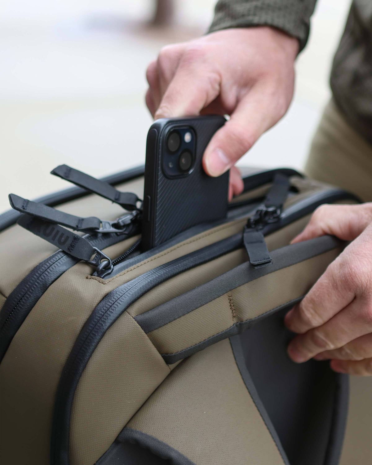 Close-up of top exterior on the Waypoint Travel Backpack in Bourbon Brown, showing accessory storage pocket with exterior zipper 