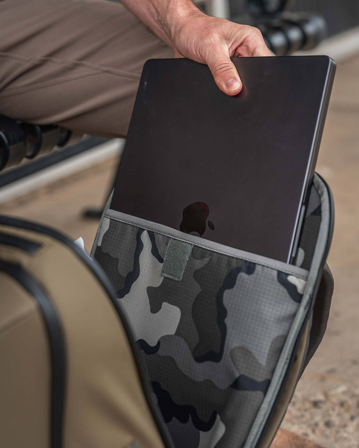 A person pulling a black laptop from the back compartment of a Waypoint Travel Backpack in Bourbon Brown.