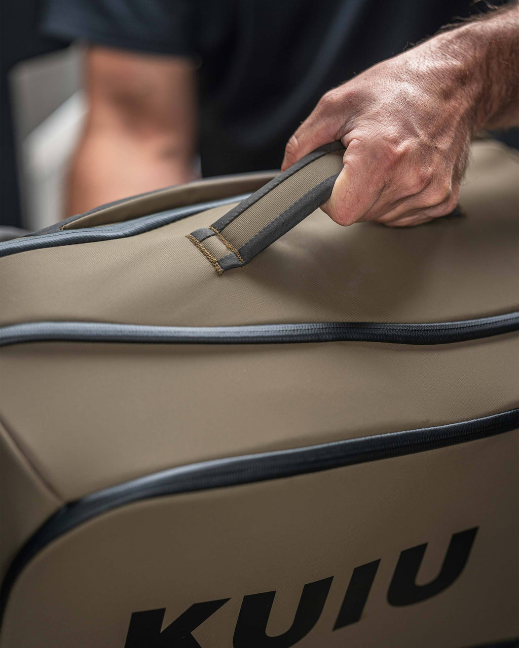 Close-up showing a person utiliizing the grab handle on a Bourbon Brown Waypoint Travel Backpack.